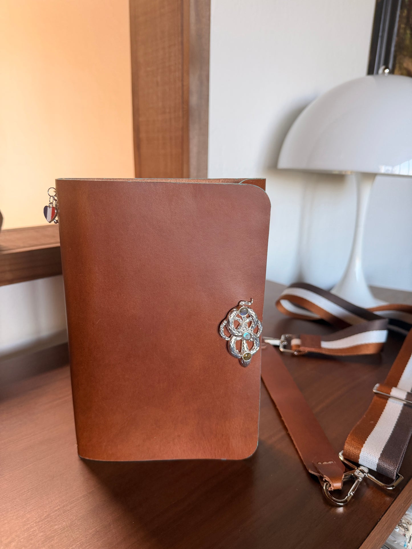 Brown leather notebook with decorative snake clasp on a wooden surface