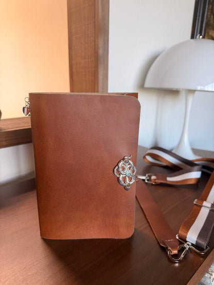 Brown leather notebook with decorative snake clasp on a wooden surface