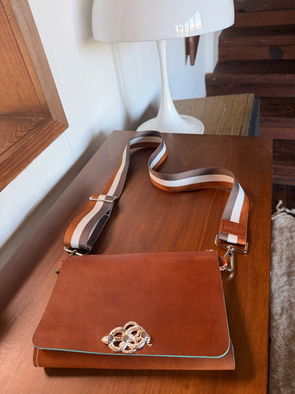 Brown leather wearable journal with decorative snake clasp on a wooden surface