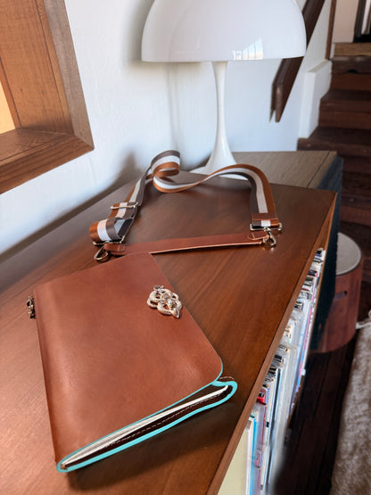 Brown leather journal on a wooden surface with a decorative snake buckle and a lamp in the background
