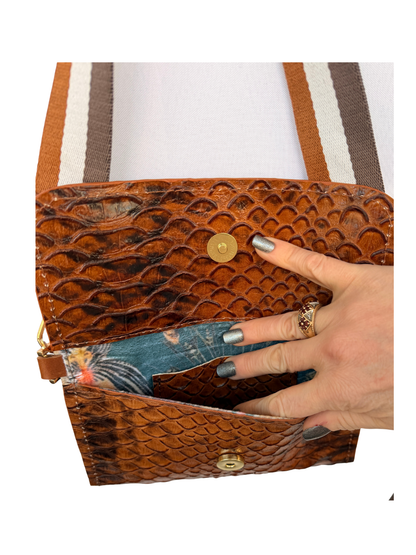 Brown textured handbag with a hand opening it, on a white background