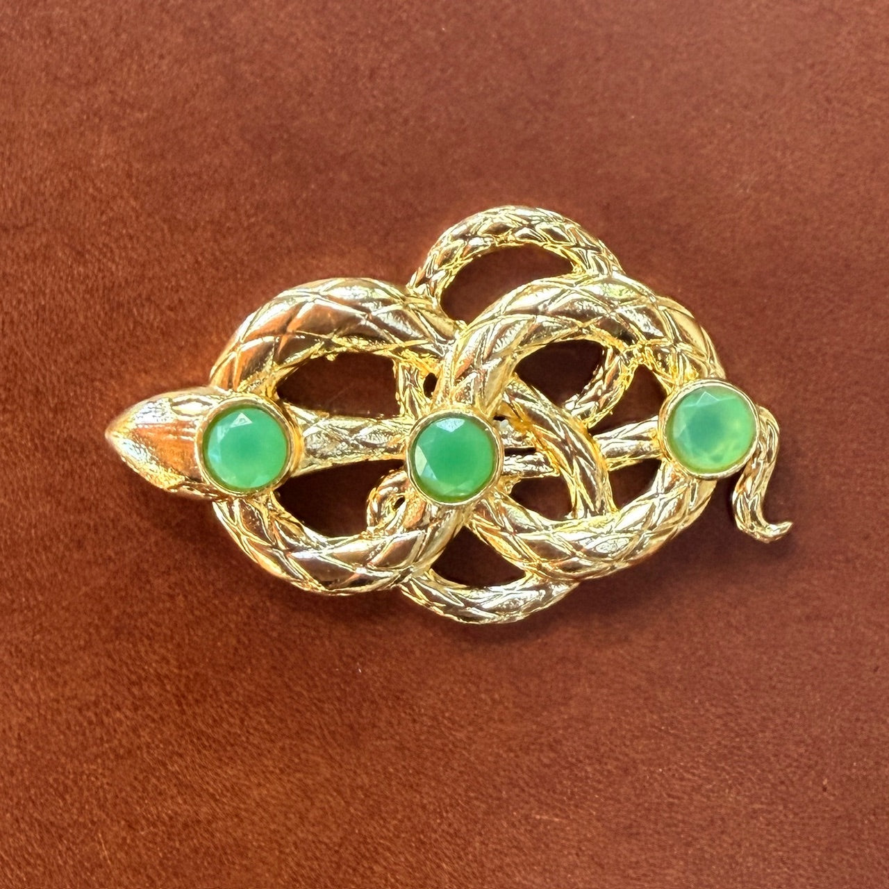 Gold snake clasp with green gemstones on a brown leather background
