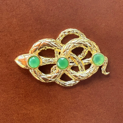 Gold snake clasp with green gemstones on a brown leather background