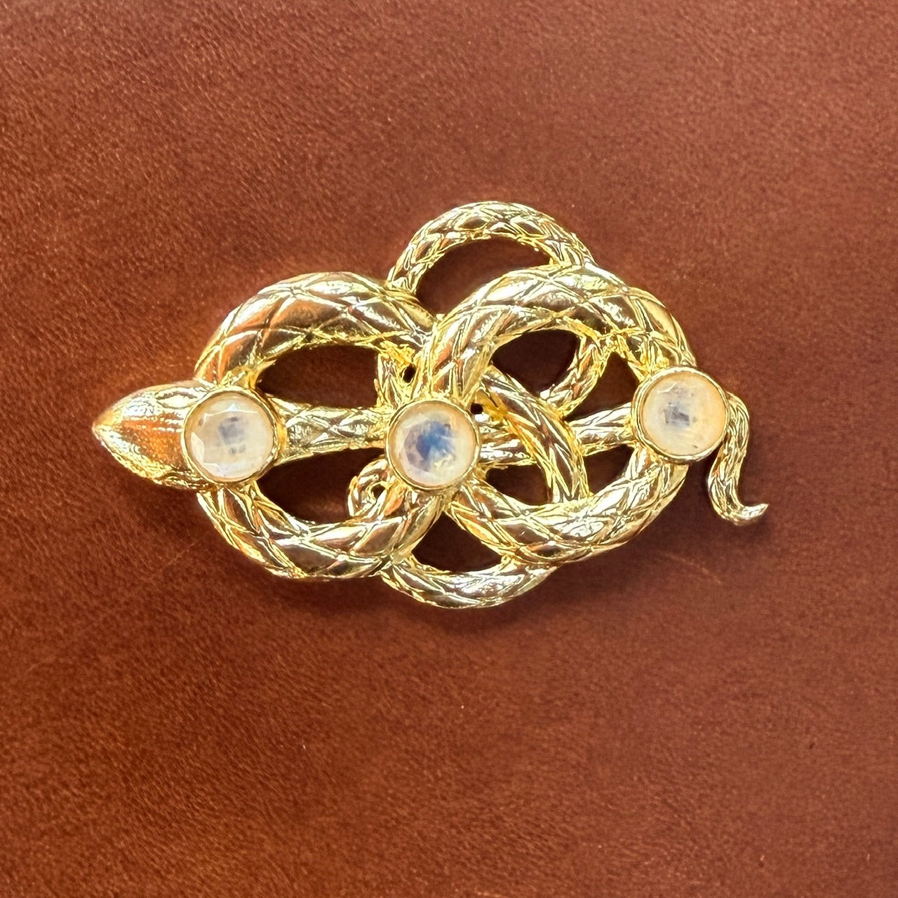 Gold snake clasp with three gemstones on a brown leather background