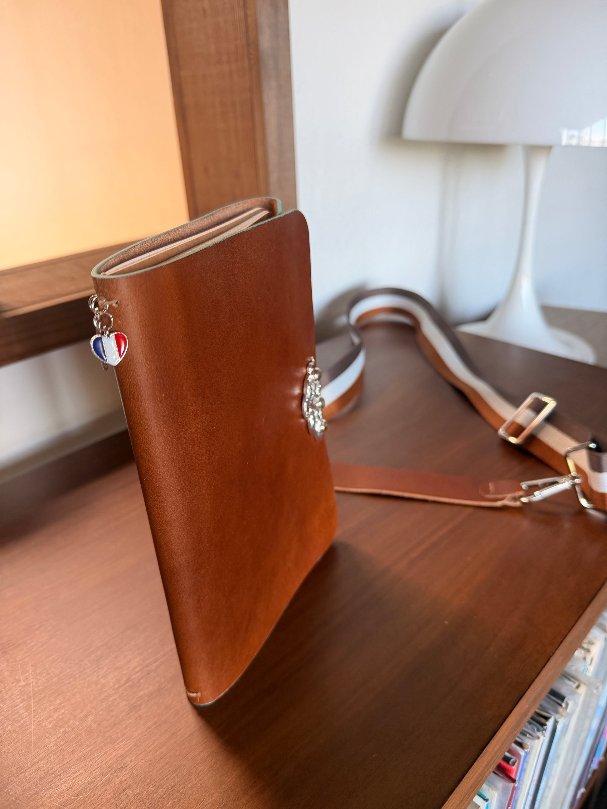 Brown leather journal with decorative snake clasp and charm on a wooden surface